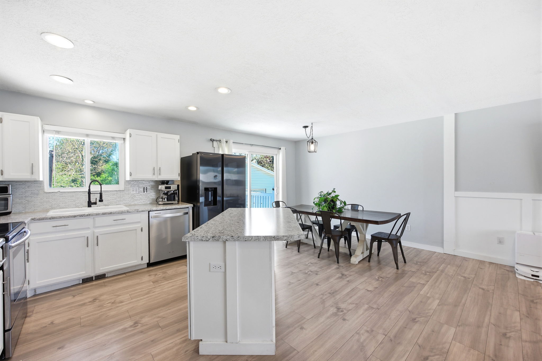 Open-concept kitchen and dining area featuring light wood-finish flooring, white cabinetry, speckled countertops, and stainless steel appliances