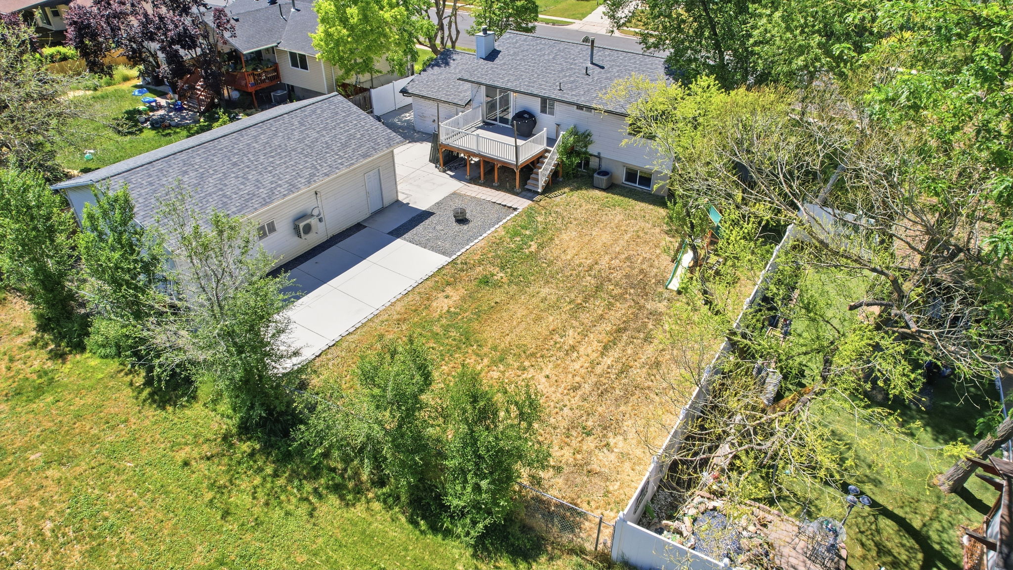 Spacious property featuring a detached garage with an extended driveway, a multi-level deck, and mature perimeter trees