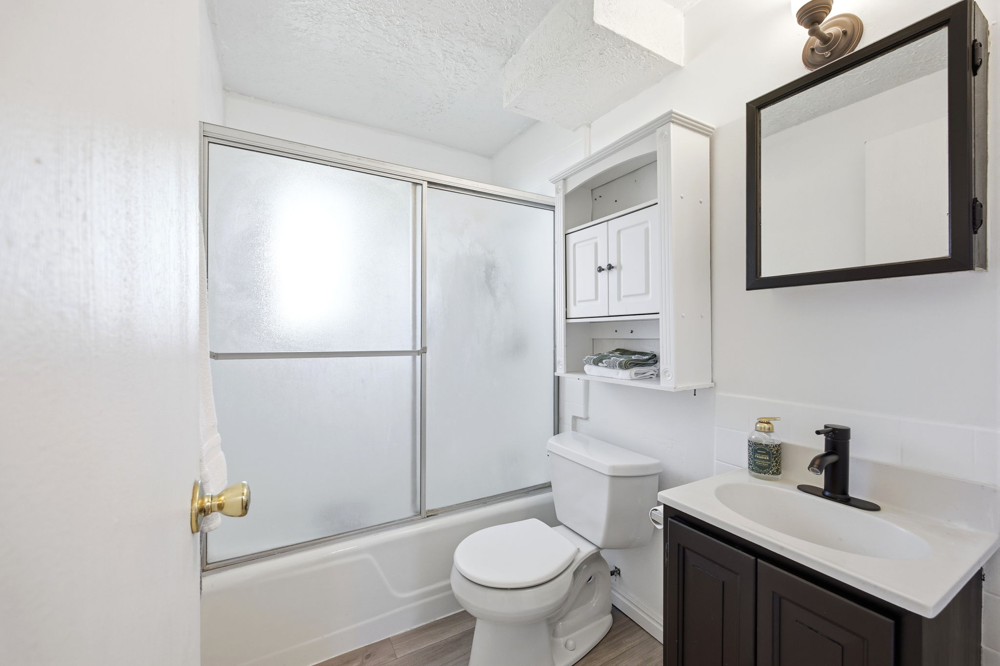 Bathroom featuring a dark wood-finish vanity with a white countertop and rectangular sink, a matte black faucet, a framed mirror, and a white wall-mounted cabinet