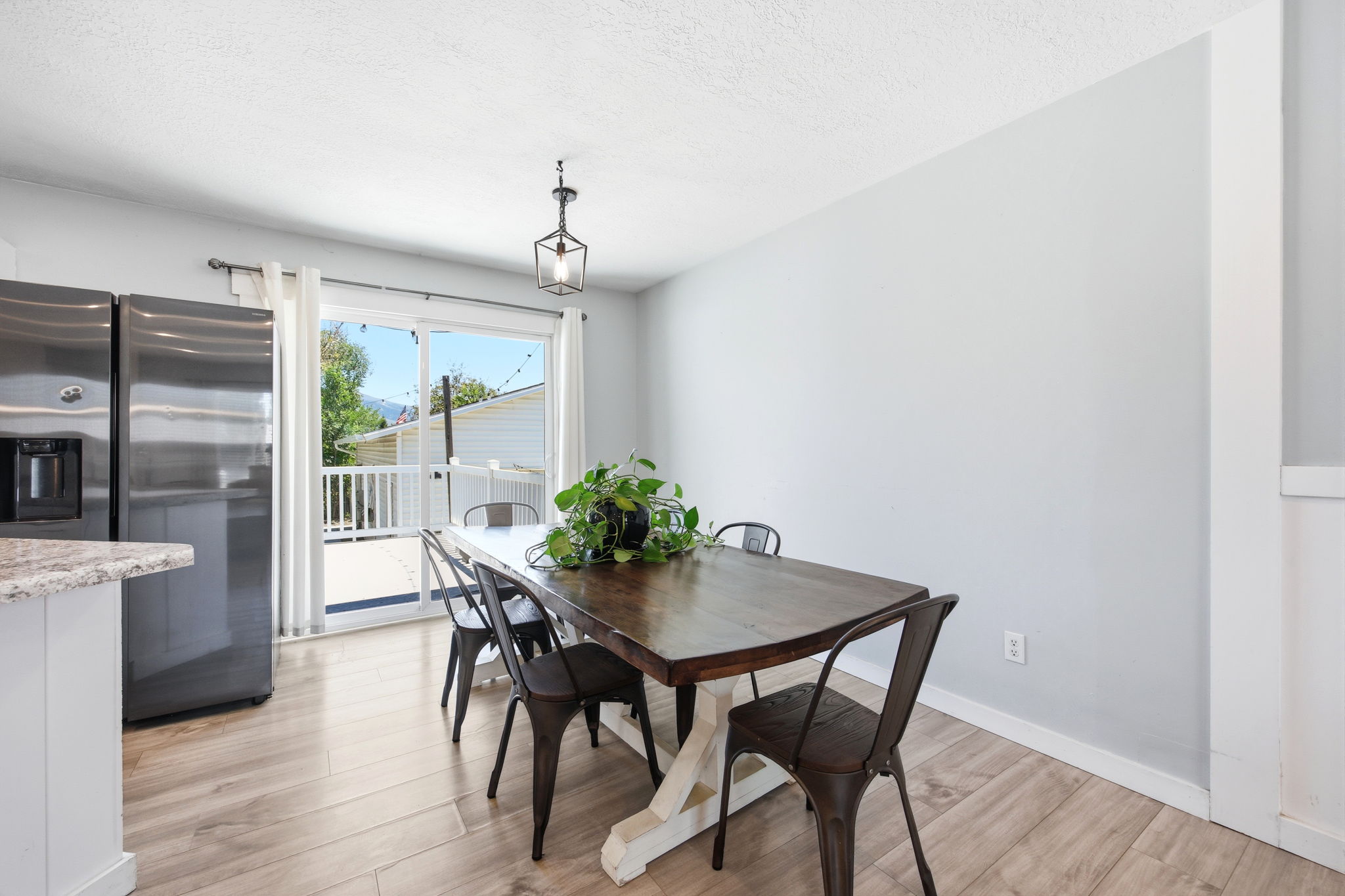 Open-concept dining area featuring wood-finish flooring, a contemporary pendant light fixture, and a sliding glass door providing exterior access