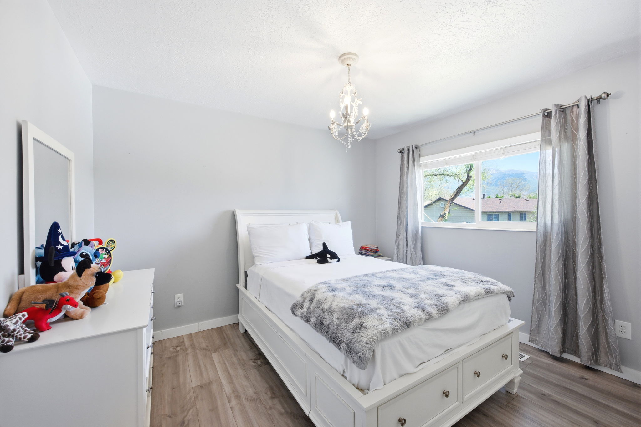 Bright room featuring wood-finish flooring, a window with exterior scenery, light gray walls, white trim, and a decorative chandelier light fixture