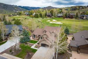 Mountainous landscape featuring a residential property with a multi-gabled roof, stone and siding exterior, and an integrated garage