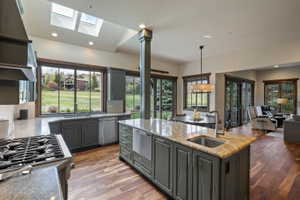 Spacious kitchen featuring an island with an undermount sink and stone countertop, stainless steel appliances, wood-finish flooring, and multiple skylights