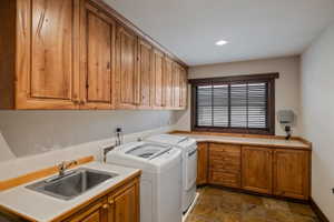Utility room featuring extensive wood cabinetry, a stainless steel sink, light-toned countertops, a window with horizontal blinds, and recessed lighting