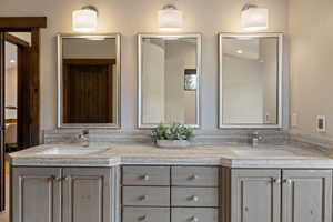 Dual vanity featuring integrated sinks, gray-toned cabinetry with varied storage, and a stone-finish countertop