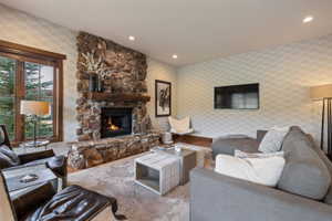 Living area featuring a stone-clad fireplace with a substantial wood mantel, a large window with wood trim, recessed lighting, and patterned wall covering