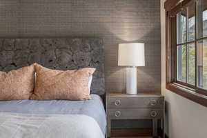 Feature wall with textured wallpaper, custom wood-slice headboard, dark-stained wood window trim, and a two-drawer nightstand with ring pulls