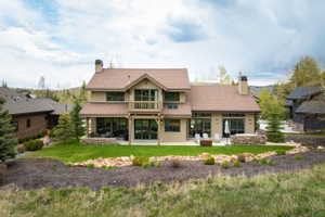 Modern mountain-style residence featuring a prominent balcony, multiple large windows, and a spacious rear patio