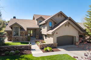 Distinguished home exterior featuring a stone and board-and-batten facade, a prominent arched garage door, a covered entry with glass-paned double doors, and a stone retaining wall bordering the front walkway