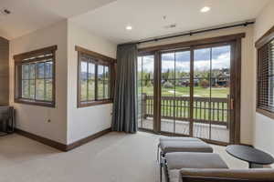 Room featuring a sliding glass door opening to a private deck, multiple windows with dark wood trim, recessed lighting, and light-toned carpet flooring