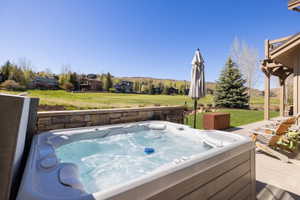 Outdoor spa tub with surrounding stone wall, concrete patio, and expansive green lawn