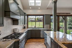 Kitchen featuring wood-finish flooring, skylights, dark cabinetry, and light-toned backsplash tiling