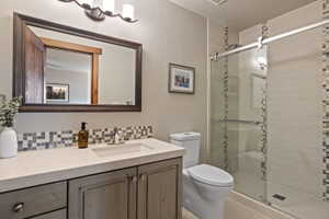 Bathroom featuring a single vanity with an integrated sink, a mosaic tile backsplash, a dark wood-framed mirror, and a glass-enclosed shower with tile surround and mosaic accents