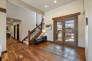 Foyer featuring double glass-paned doors, a tile entry, wood-finish flooring, and a staircase with dark wood railings and carpeted treads