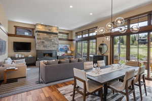 Spacious open-concept living area featuring a stone fireplace, wood-finish flooring, and expansive glass doors