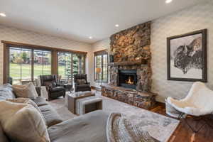 Living room featuring a stone fireplace with a wood mantle, hardwood flooring, recessed lighting, and large windows with wood trim