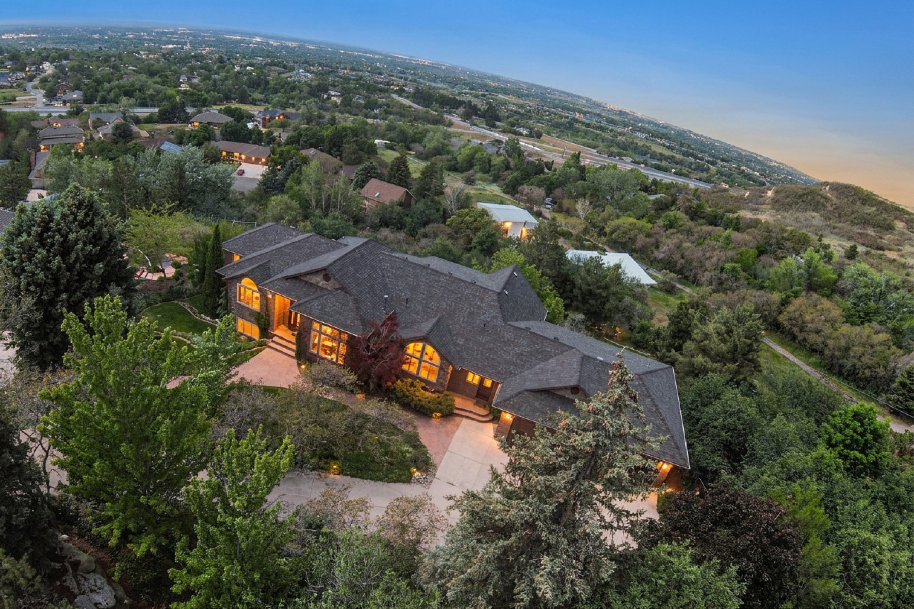 Sprawling architectural residence featuring a multi-gabled roofline, abundant mature landscaping, and an extensive paved drive