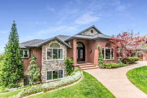 Brick and stone exterior featuring an arched entryway with a decorative glass door, a paved walkway, a shingled roof, and mature landscaping