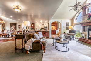 Open-concept living area featuring a stone fireplace with wood mantel, a large arched window, vaulted ceilings, and recessed lighting, dark wood hearth.