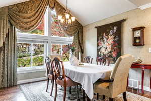 Dining area featuring a vaulted ceiling, a multi-pane picture window, wood-finish flooring, and a decorative chandelier