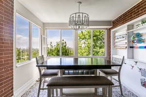 Dining area featuring a dark-toned table, a contemporary chandelier, large windows, exposed brick accents, and patterned floor tiling