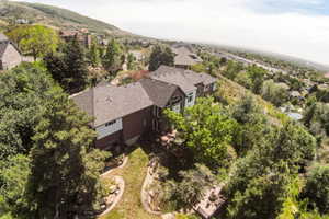 Hillside property featuring a multi-level design, a dark shingle roof, and a terraced backyard with mature trees