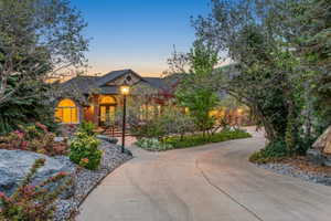 Paved driveway framed by mature trees, leading to a stone and brick facade residence