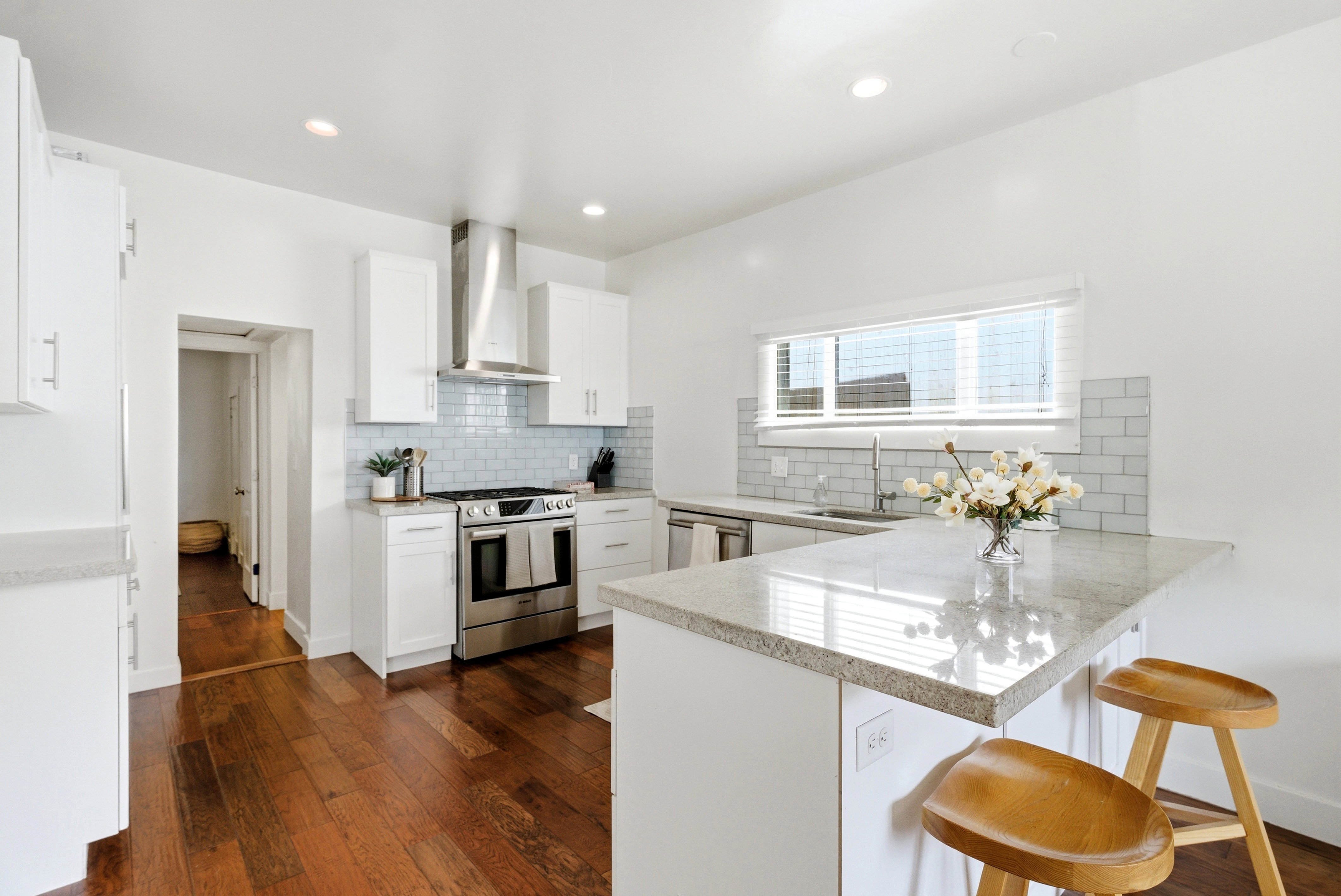Kitchen featuring wood-finish flooring, white cabinetry, a light-toned countertop, subway tile backsplash, and stainless steel appliances