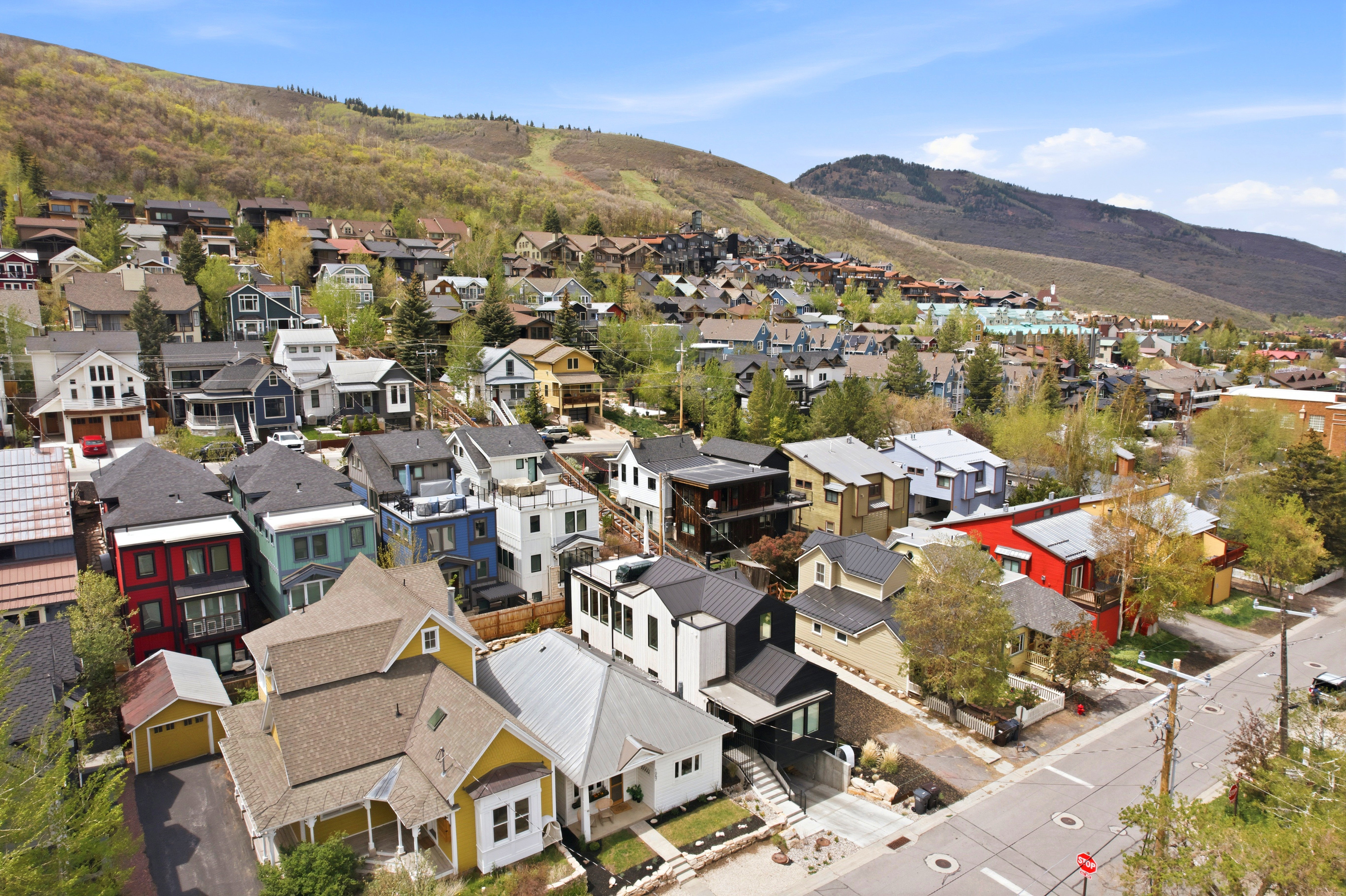 Elevated neighborhood setting featuring diverse architectural styles, visible roadways, surrounding hillsides with natural vegetation, and distant town elements