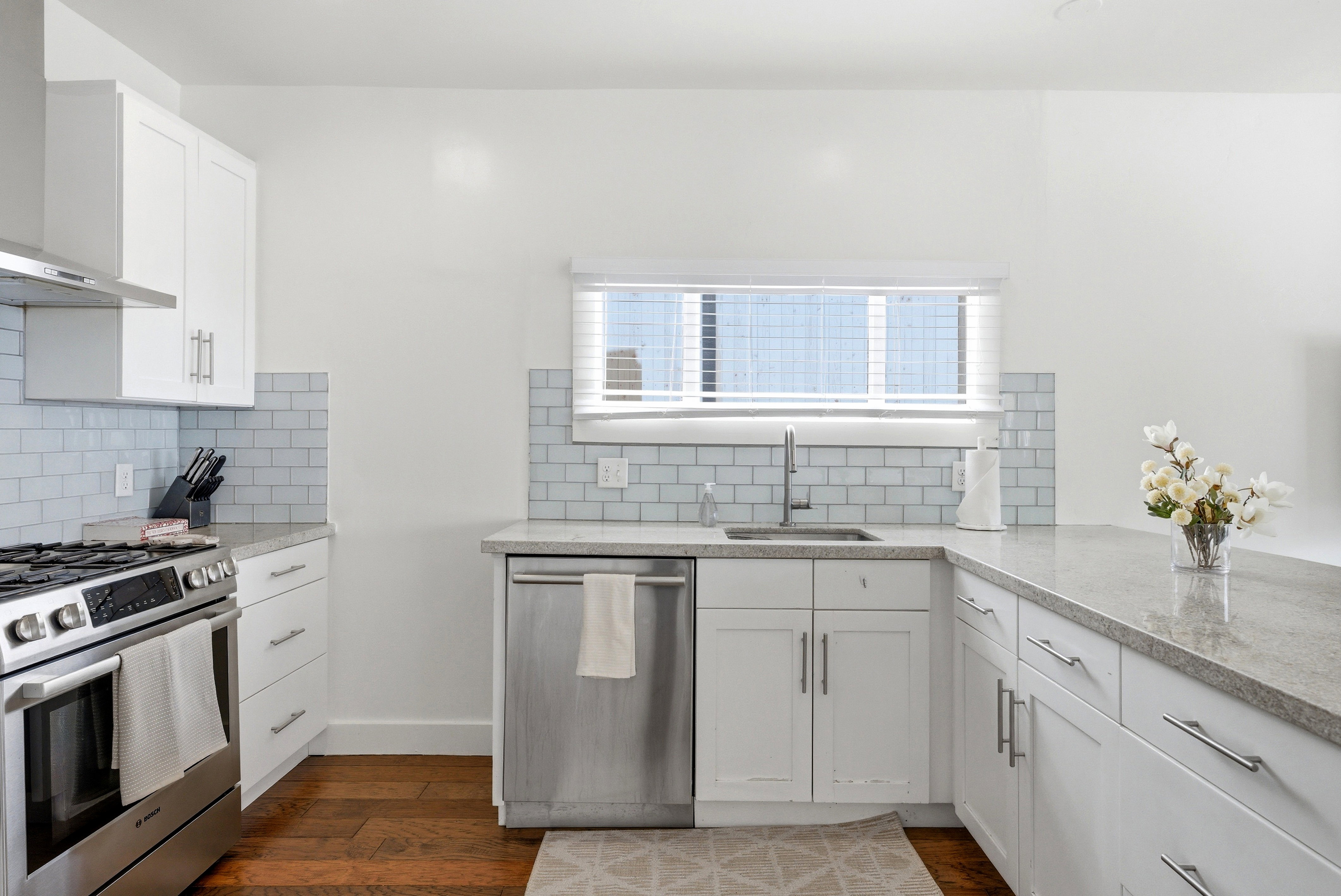 Kitchen featuring white shaker cabinetry, stainless steel appliances, light-toned countertops, and a subway tile backsplash