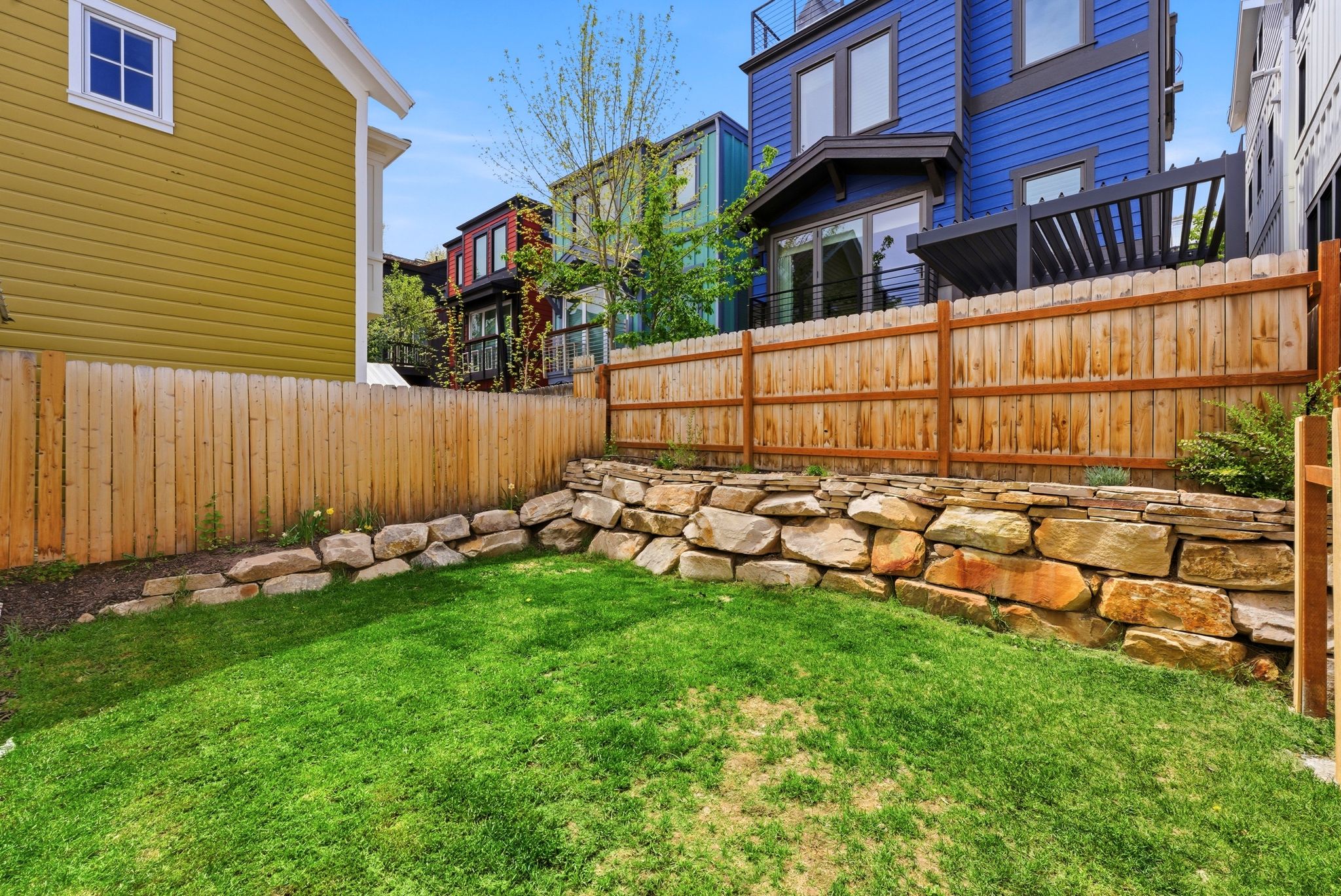 Private, fenced yard with a stone retaining wall and lush green lawn