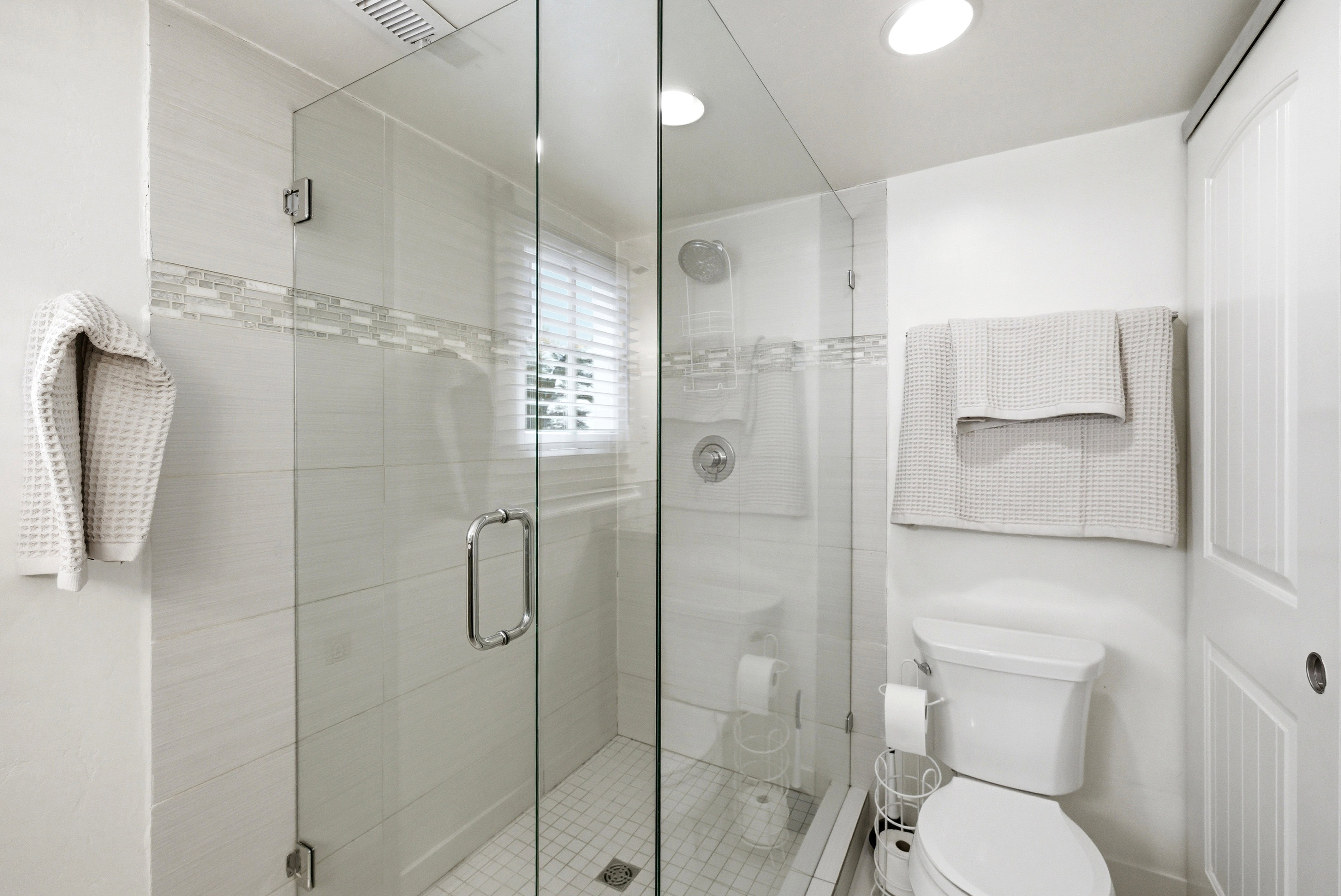 Walk-in shower with clear glass enclosure, subway tile surround, and decorative mosaic accent band