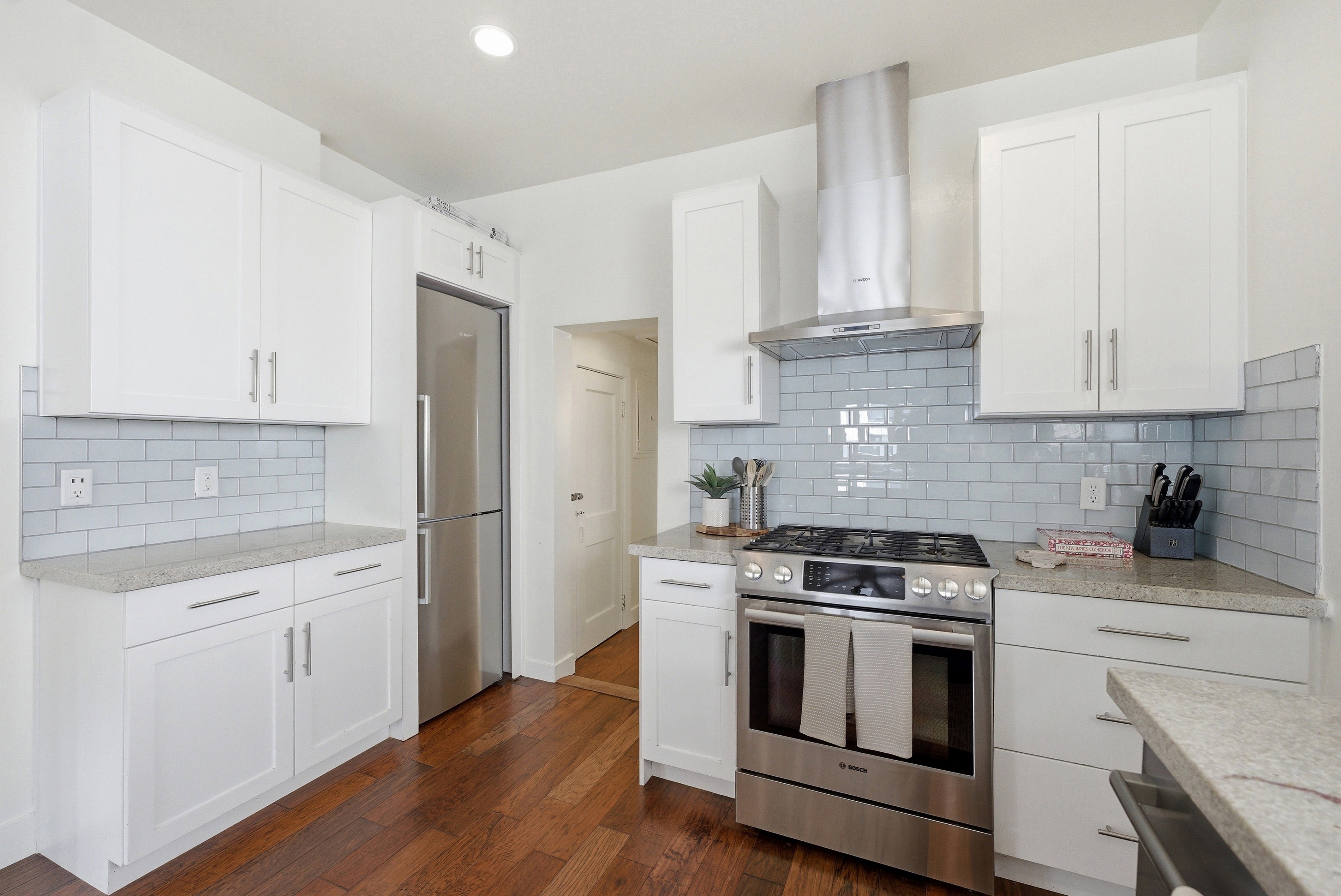 Kitchen featuring white cabinetry with brushed nickel hardware, stainless steel appliances, light blue subway tile backsplash, and light-toned countertop surfaces