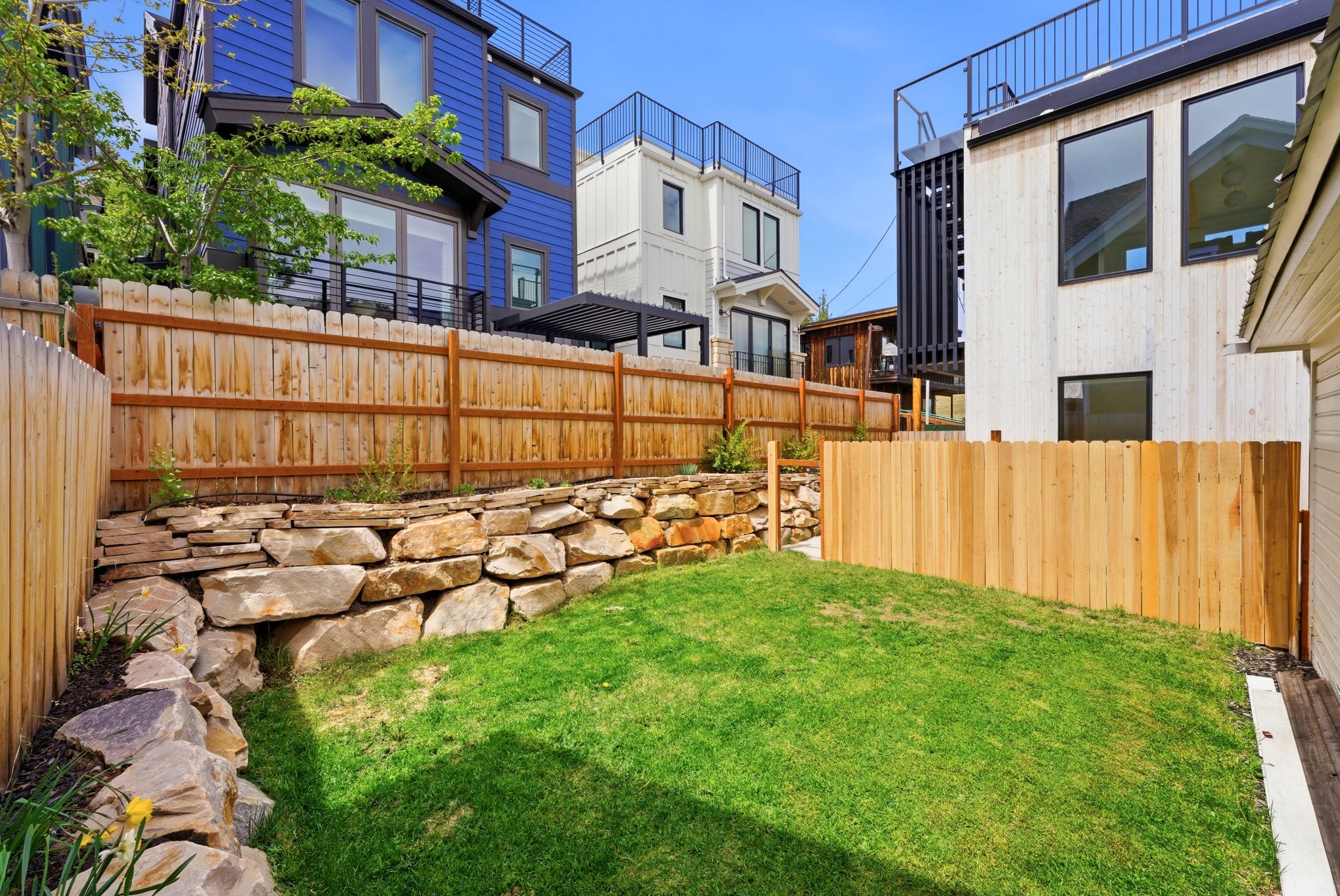 Terraced backyard featuring a manicured lawn, natural stone retaining wall, and wood privacy fencing