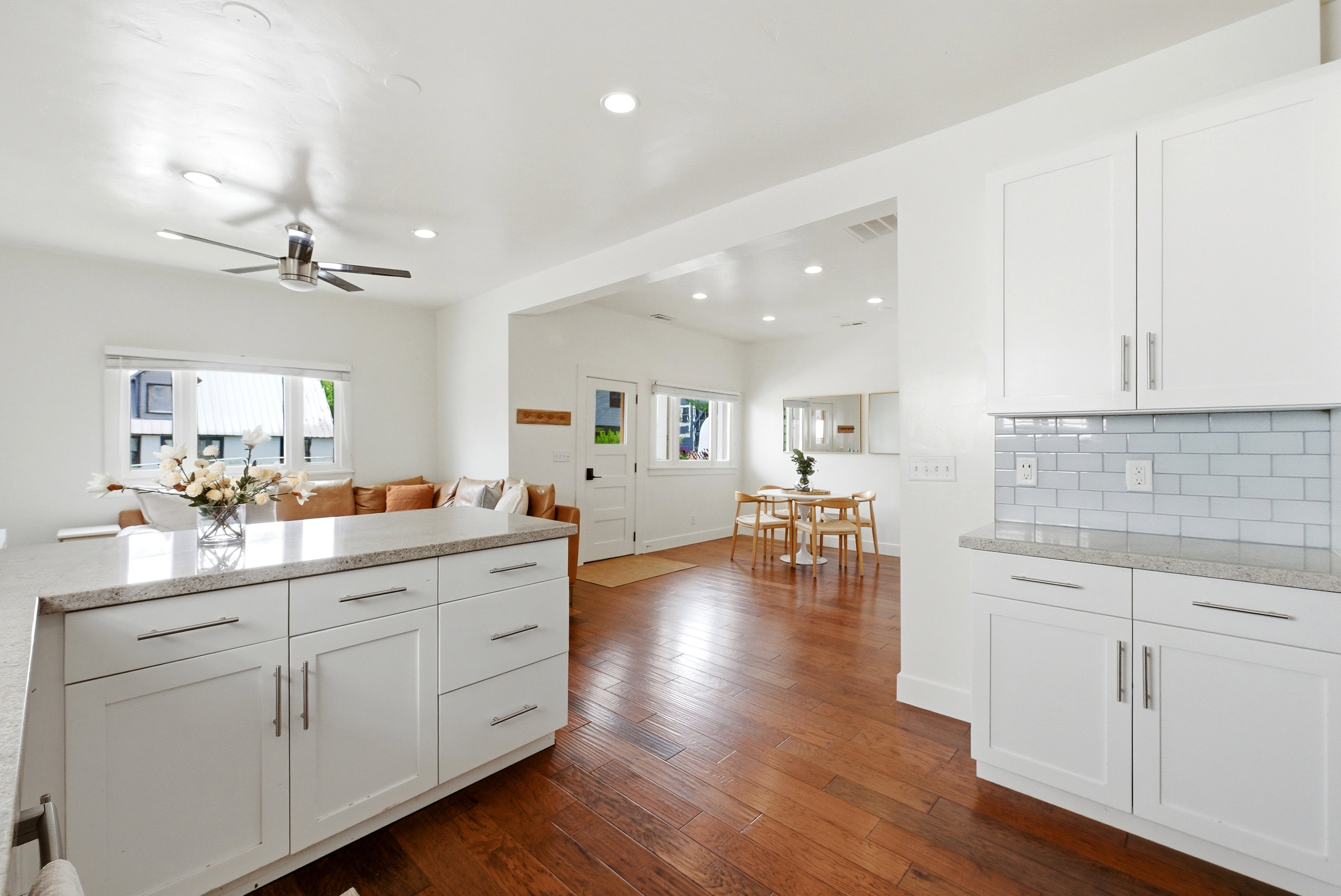 Kitchen featuring a large island with stone countertop, white shaker cabinetry, stainless steel hardware, and subway tile backsplash