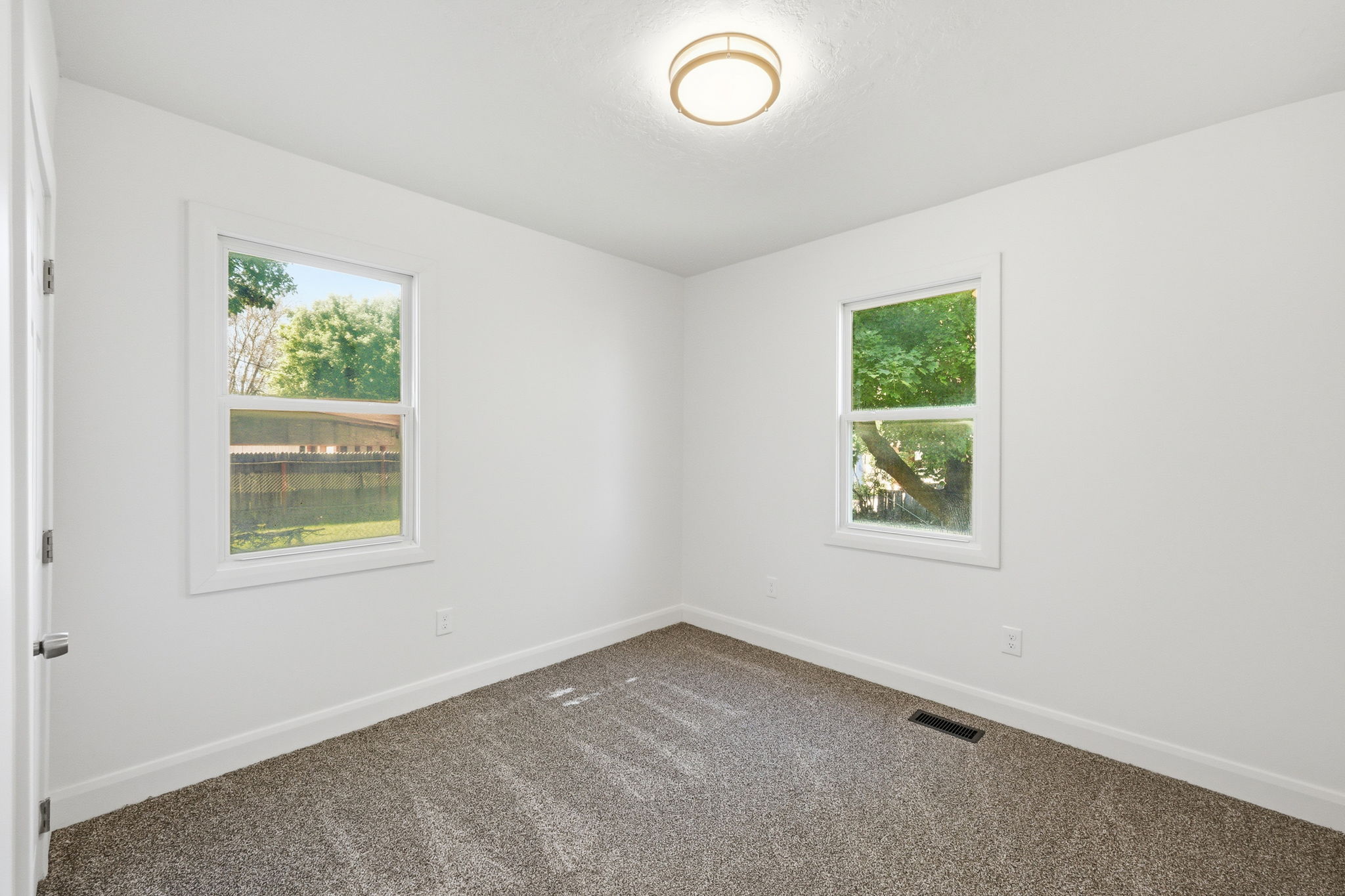 Bright interior space featuring two windows with white trim, a flush-mount ceiling light, and neutral-toned carpeting