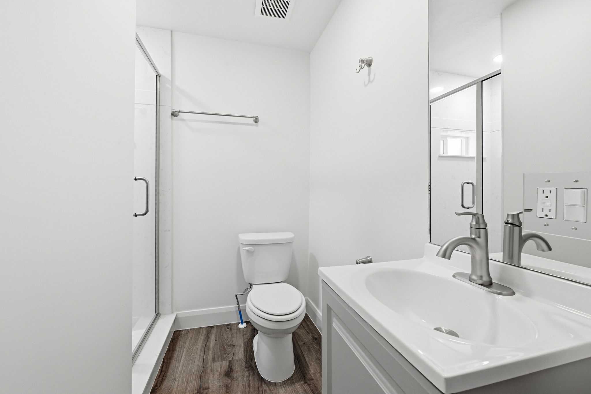 Bathroom featuring a glass-enclosed shower, wood-finish flooring, a white vanity with an integrated sink, a brushed nickel faucet, and a wall-mounted mirror