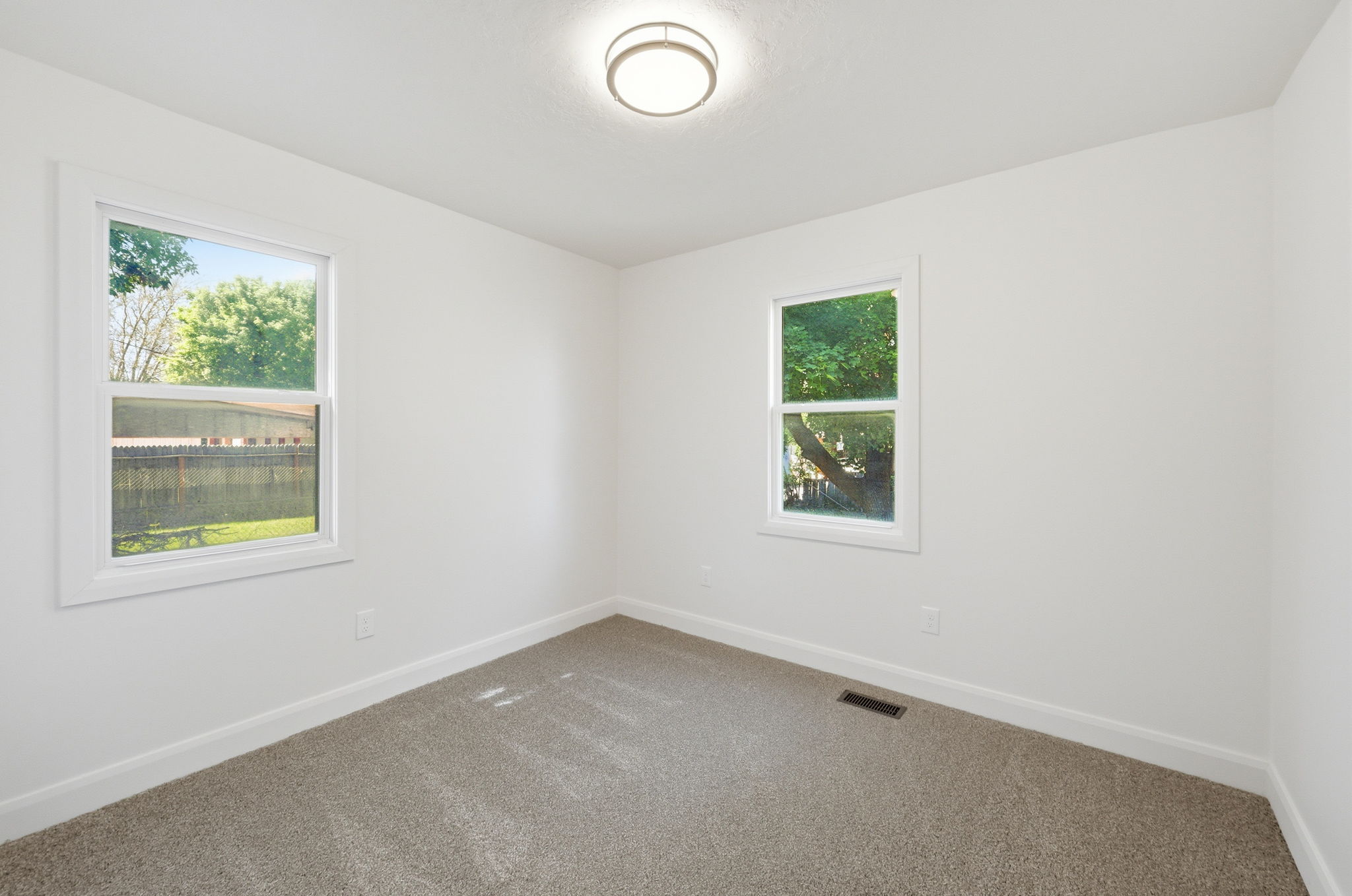 Bright room featuring two windows with white trim, neutral carpet flooring, and a flush mount ceiling light fixture