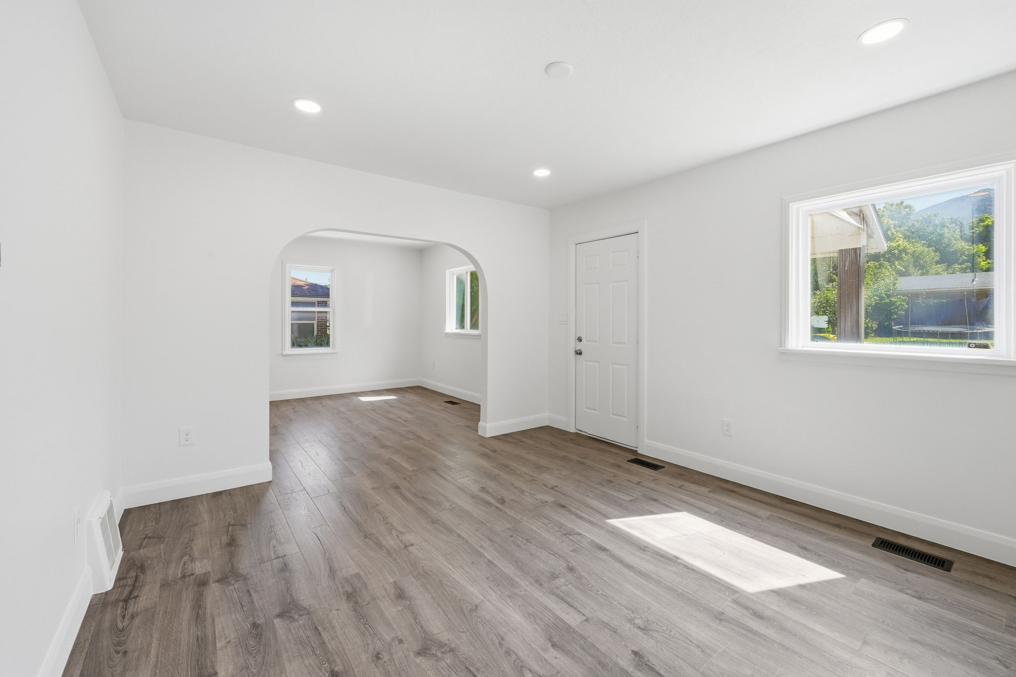 Open concept living area featuring wood-finish flooring, recessed lighting, white baseboards, and a white paneled entry door