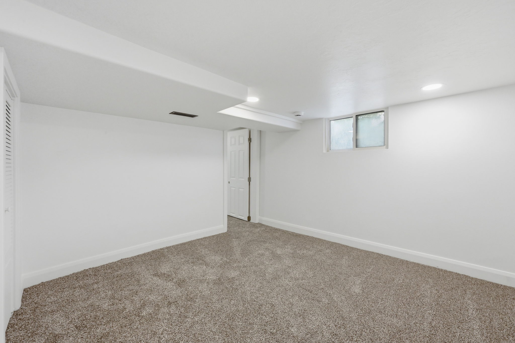 Spacious room featuring neutral carpeting, white walls, recessed lighting, and a white interior door