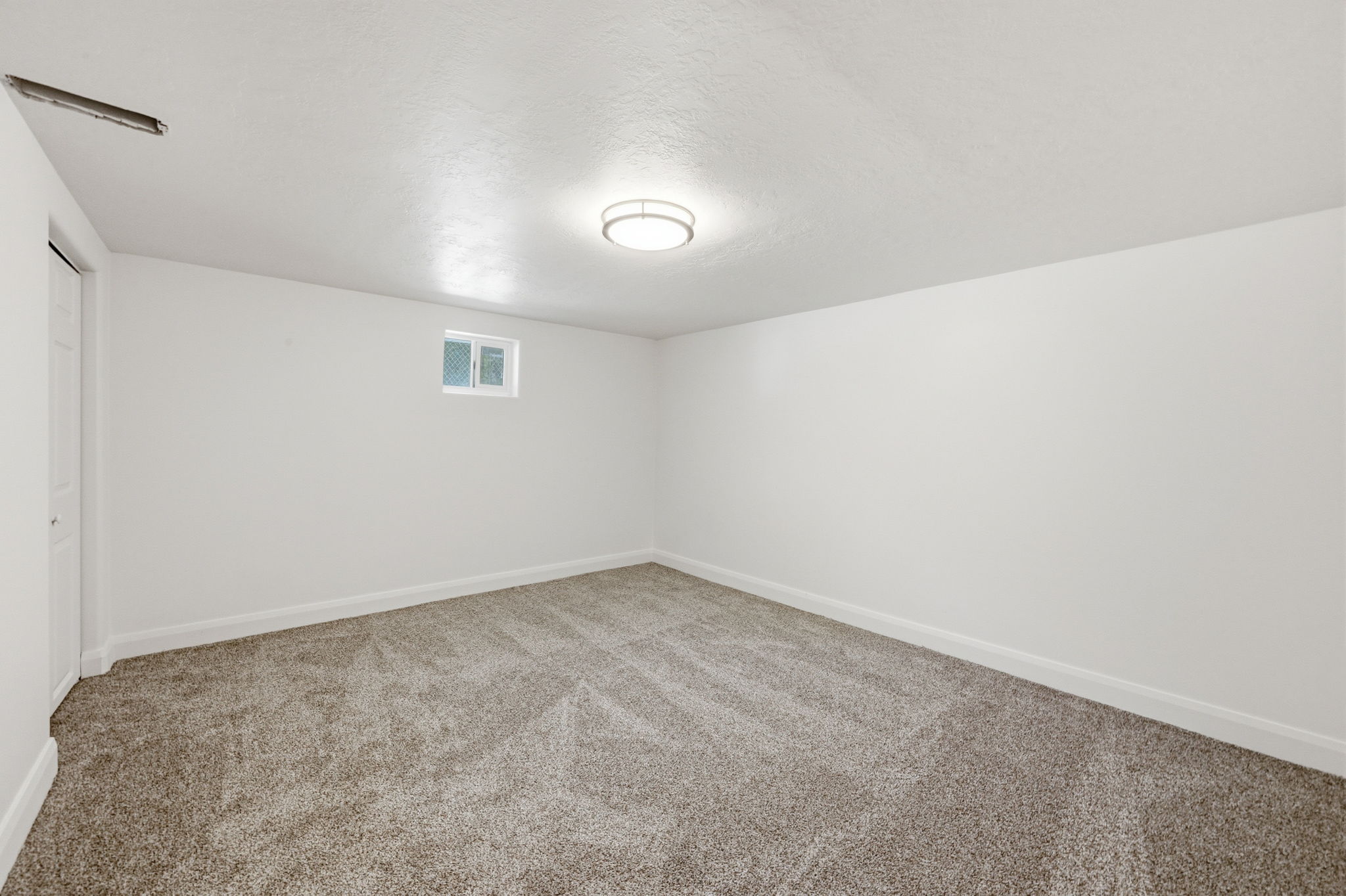 Spacious room featuring new carpeting, a fresh white paint scheme, a flush-mount ceiling light fixture, a window providing natural illumination, and a white interior door