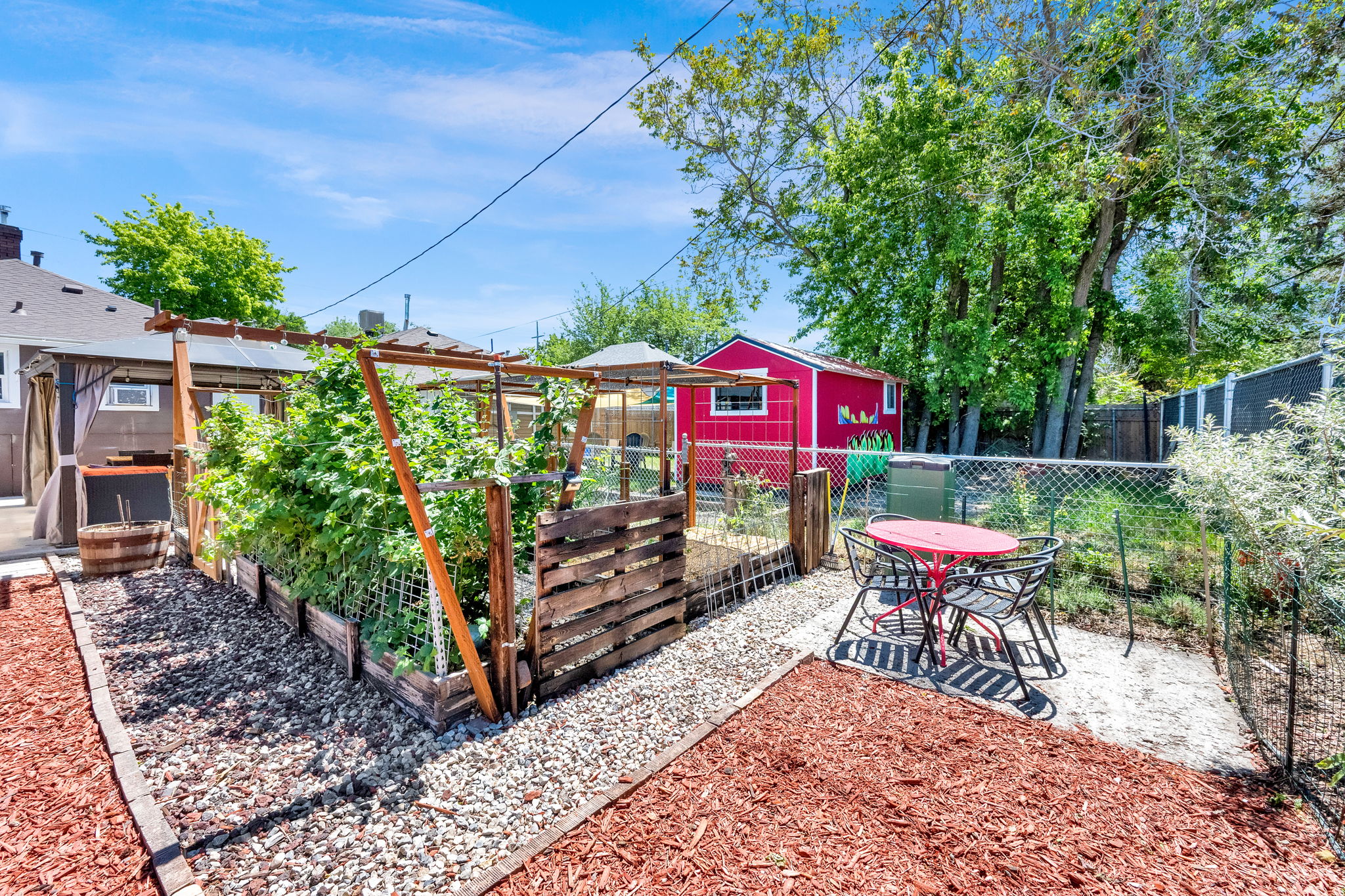 Expansive backyard featuring a dedicated garden area with trellises and raised beds, a gravel pathway, a red storage shed, and mature trees