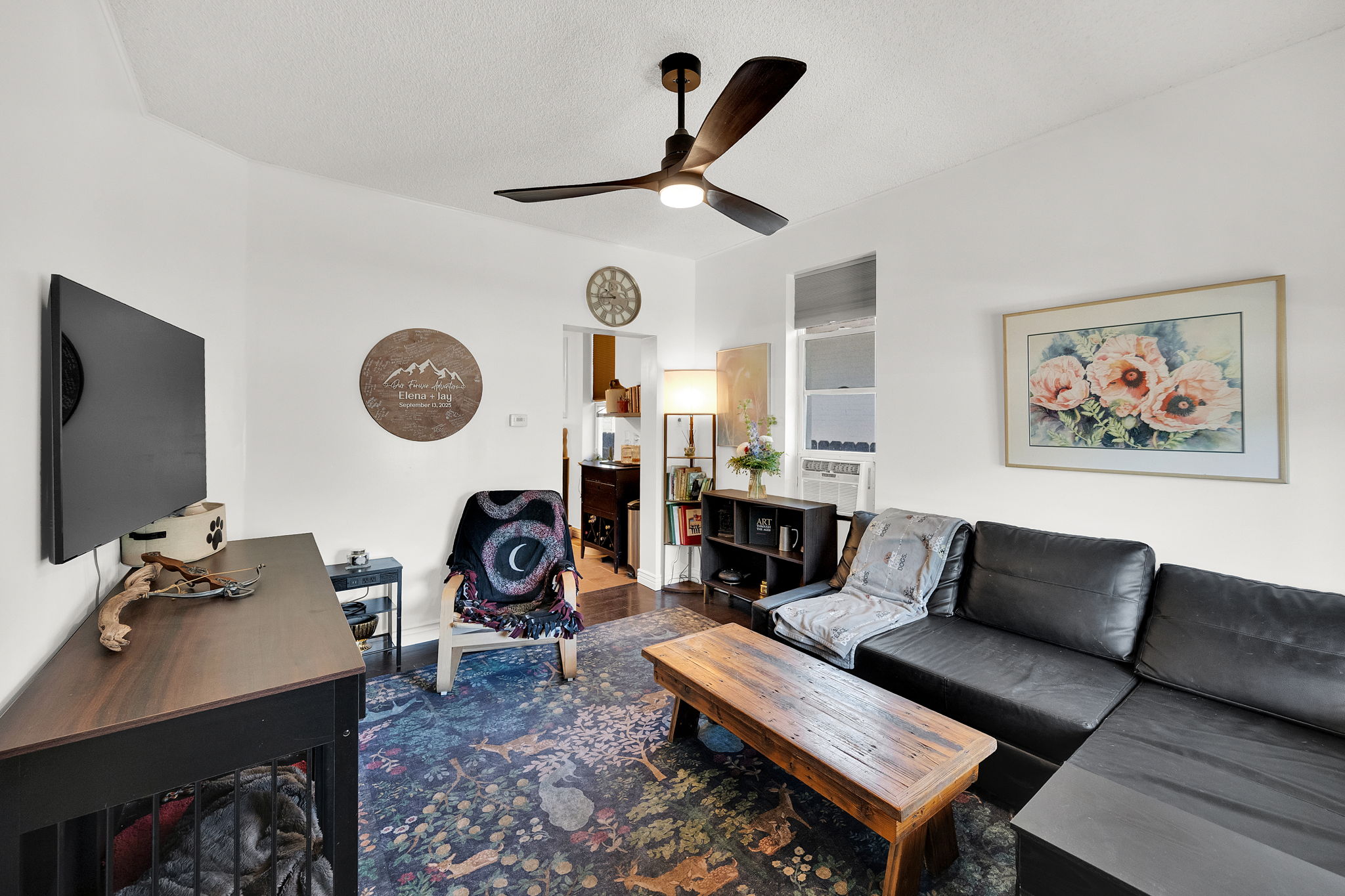 Living area featuring a ceiling fan with integrated lighting, white walls, and a window providing natural light