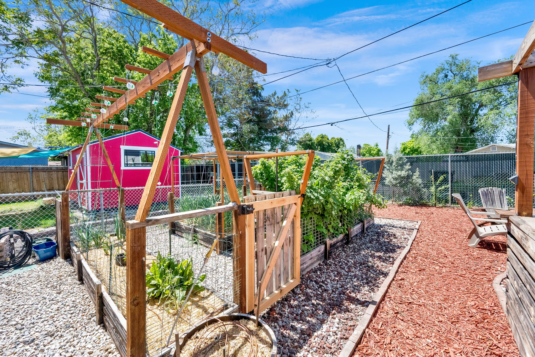 Fenced garden beds featuring wood and wire construction, a wooden gate, and an overhead trellis system