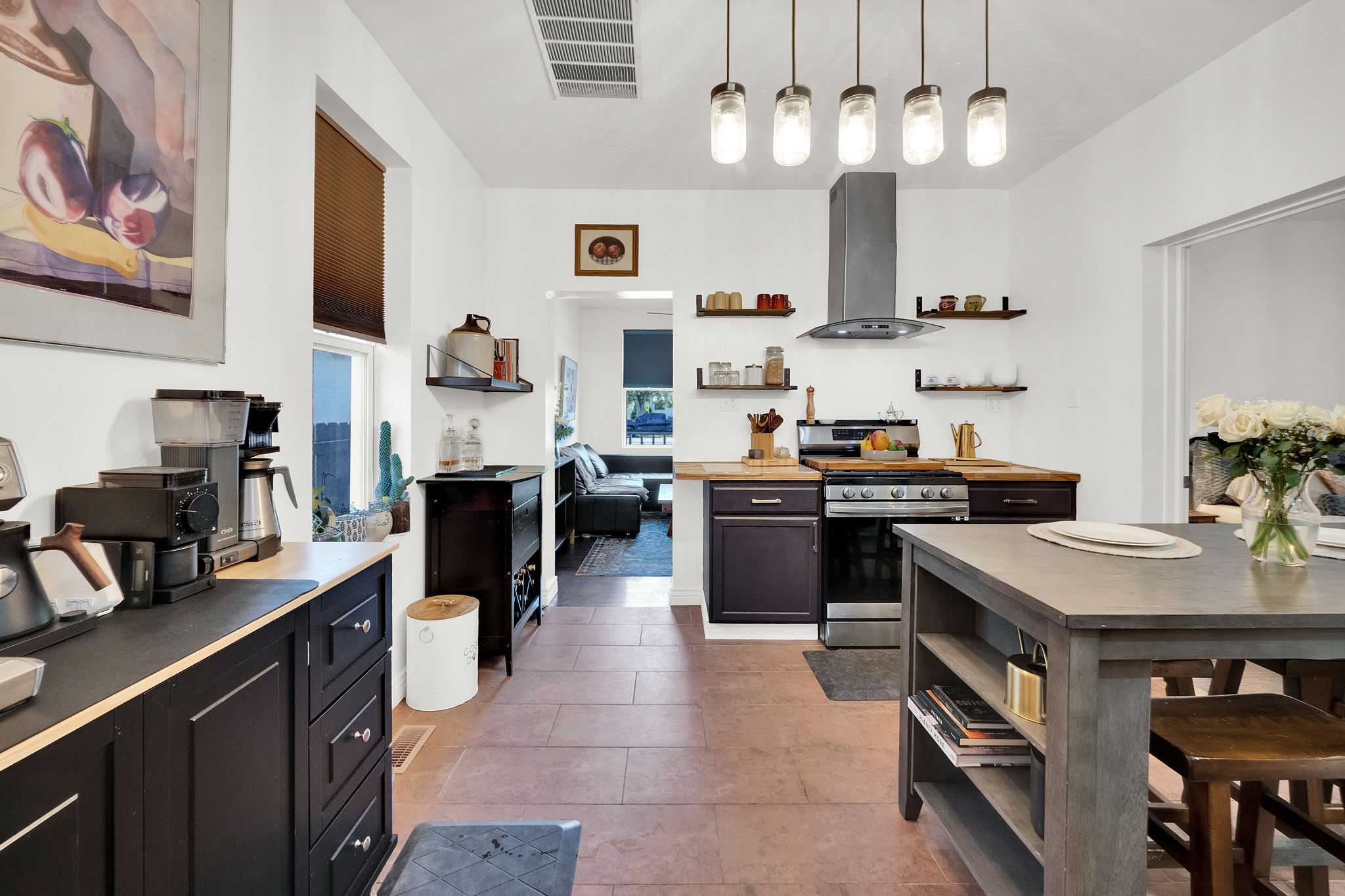 Spacious kitchen featuring stone flooring, dark wood-finish cabinetry, a stainless steel range with overhead vent hood, and an eat-at island