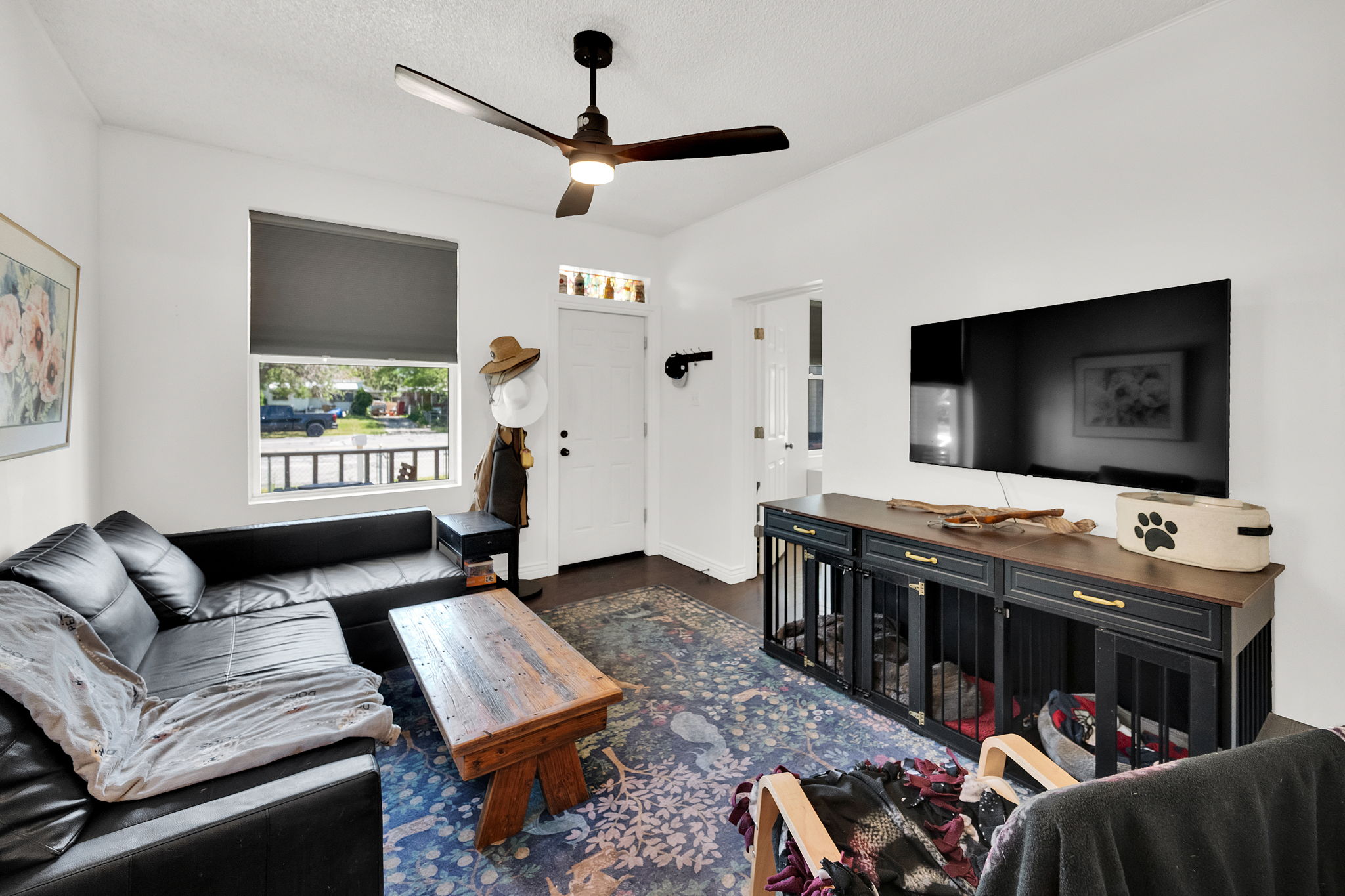 Inviting living area featuring a ceiling fan, a window with a roller shade, and a white entry door with decorative glass