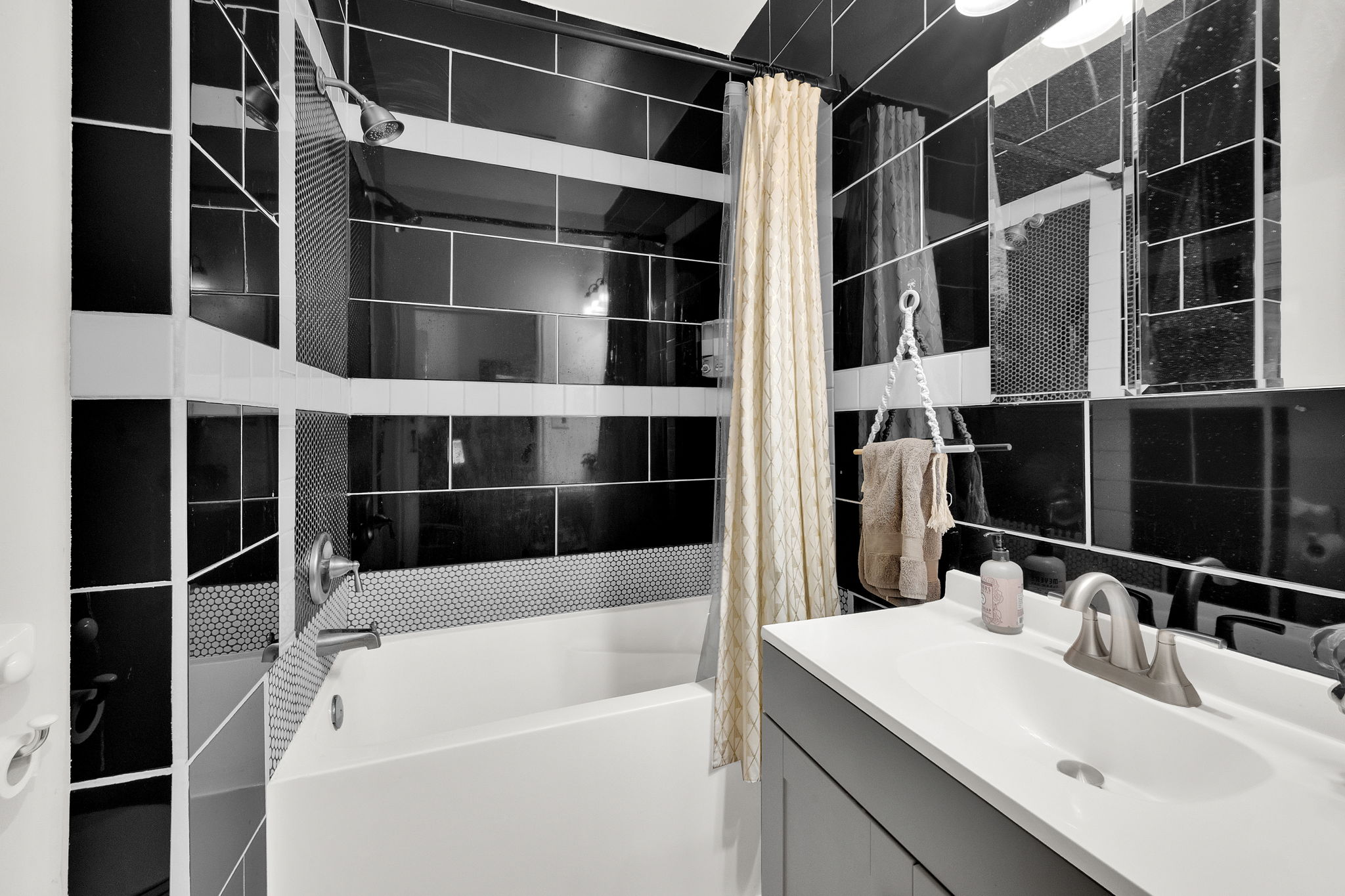 Full bathroom featuring a tub/shower combination with black subway tile and penny tile accents, a single vanity with a white countertop and basin, and a mirrored medicine cabinet