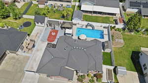 Aerial view showcasing a rectangular swimming pool with a slide, an enclosed sports court, a paved driveway, and multiple outbuildings