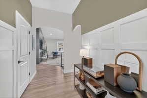 Entryway featuring wood-finish flooring, white wainscoting, and an arched doorway