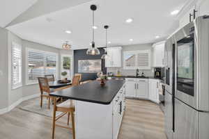 Modern kitchen featuring white cabinetry, a large island with a dark countertop, stainless steel appliances, and wood-finish flooring